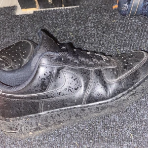 Svarta Nike Air Force 1 sneakers - Dem är slitna. Säljer ett par klassiska svarta Nike Air Force 1 sneakers med låg profil. Skorna har snörning, perforerad tå och platt sula. Tillverkade i skinn med detaljer i textil runt ankeln. Snygg och tidlös design som alltid funkar.