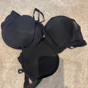 3-pack, Svart vadderad bh 75B - Svart vadderad bh från ECO, och någon är från H&M, i storlek 75B. Bh:n har släta kupor, justerbara axelband och stängning bak. Sidorna är i mesh och materialet känns mjukt och följsamt. Perfekt för dig som vill ha en enkel och stilren bh.