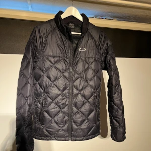 Svart quiltad jacka från Oakley - Snygg svart quiltad jacka från Oakley i fint befintligt skick. Mellan tjock. Storlek Small. 