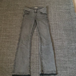 Grå bootcut jeans med fickdetaljer - Säljer ett par grå jeans med bootcut och lowwaist -modell och snygga bakfickor med knappdetaljer. Jeansen har klassisk femficksdesign och är tillverkade i mjukt denimtyg. Perfekta för dig som gillar en avslappnad men ändå trendig look. Har spretat upp dem där nere 