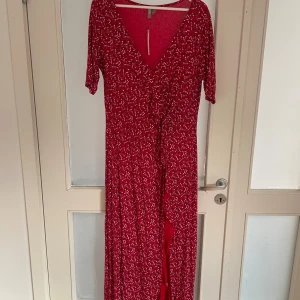 Röd blommig långklänning från ASOS - Säljer en röd långklänning från ASOS Curve med små blommor i vitt, blått och rosa. Klänningen har v-ringning, korta ärmar och en omlott-detalj framtill. Materialet är mjukt och följsamt, perfekt för dig som gillar färg och mönster.