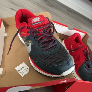 Nike Lunar Forever 4 sneakers röd/svart - Nike Lunar Forever 4 sneakers i rött och svart med silvriga detaljer och vit sula. Ovandelen är i mesh och syntet för bra andningsförmåga. Klassisk Nike-logga på sidan och snörning framtill. Perfekta för dig som gillar sportig stil och vill sticka ut.