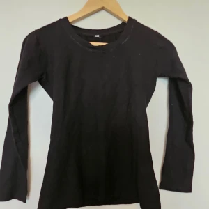 Svart långärmad tröja i bomull - En basic svart långärmad tröja i mjuk bomull. Enkel och stilren modell med rund halsringning, perfekt att matcha med jeans eller kjol. Skön passform och ett måste i garderoben för dig som gillar minimalistisk stil.