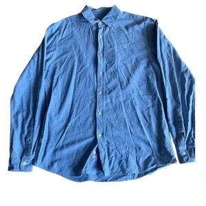 Ljusblå skjorta från Morris, storlek M - Säljer en stilren ljusblå skjorta från Morris i storlek M. Skjortan har klassisk krage, vita knappar och en liten broderad logga på bröstet. Perfekt för dig som gillar enkel och clean stil.