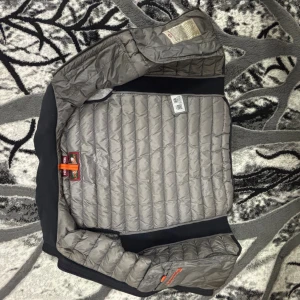 Grå dunväst från Parajumpers - Snygg quiltad dunväst från Parajumpers i grått med svarta detaljer. Västen har dragkedja framtill, två sidofickor med dragkedja och en gul detalj vid kragen. Perfekt för lager-på-lager och stilren look.