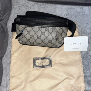 Gucci axelväska med GG-mönster - Snygg axelväska från Gucci i beige och svart med klassiskt GG-mönster. Väskan har svarta skinn-detaljer, justerbar rem och dragkedja upptill. Perfekt för att bära det viktigaste och ger en lyxig touch till din outfit.