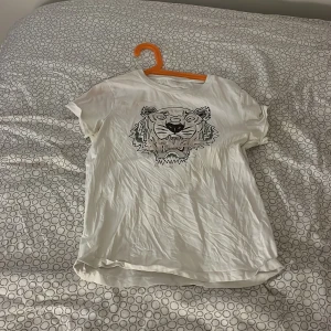 Vit Kenzo t-shirt med tigertryck - Vit t-shirt från Kenzo med ikoniskt tigertryck framtill. Klassisk rund hals och korta ärmar. Tillverkad i mjuk bomull som känns skön mot huden. Perfekt för dig som vill ha en cool och stilren look med en twist.