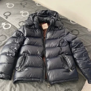 Moncler maya - Hej säljer en moncler maya eftersom att den inte passar mig storleken är M men kan också passa S färgen är navy det finns 2 defekter häng grejen är sönder men man kan säker fixa den och snöret har gått sönder men kan säkert fixas någonstans det är därför jag säljer den för billigt 