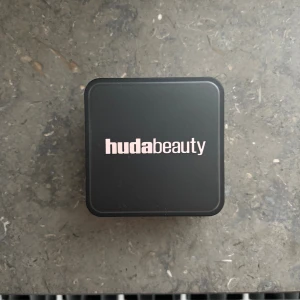 Huda Beauty Cherry Blossom Cake puder - Loose Baking & Setting Powder i färgen Cherry Blossom Cake från Huda Beauty. Kommer i en kvadratisk plastburk med svart lock och rosa puder inuti. Perfekt för att sätta sminket och få en flawless finish. Innehåller 20g. Snygg och trendig design.
