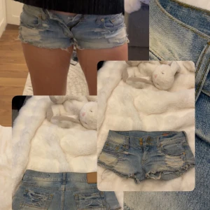 Blå slitna jeansshorts med fransar - Säljer ett par ljusblå jeansshorts med låg midja och råa, fransiga kanter. Shortsen har slitna detaljer både fram och bak, dubbla knappar i midjan och klassiska fickor. Perfekta för sommaren och ger en cool, avslappnad vibe.