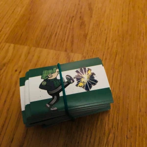 Bajen klibbor  - En bunt kort med tecknade illustrationer av en person i sportkläder som sparkar en symbol, troligen relaterad till fotboll. Perfekt för dig som gillar sport och samlar på unika kort! Passar ungdomar och unga vuxna med intresse för fotboll och roliga illustrationer.