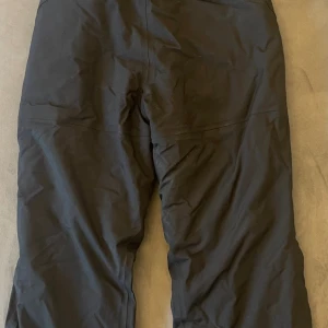 Svarta täckbyxor Polarn O. Pyret 152 - Svarta täckbyxor från Polarn O. Pyret i storlek 152. Har hängslen. Byxorna är tillverkade i slitstarkt syntetmaterial och har en klassisk rak passform. Perfekta för kalla dagar och vinteraktiviteter. Snygg och enkel design utan onödiga detaljer.