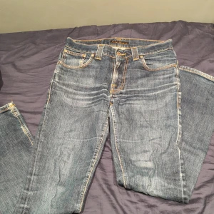 Blå jeans från Nudie med kontrastsömmar - Säljer ett par klassiska blå jeans från Nudie i modellen Grim tim. Jeansen är i storleken 28/32 men kan även passa 27/30. Jeansen har en liten defekt mellan bena och därför säljer jag billigt. Nypris är cirka 1699kr 