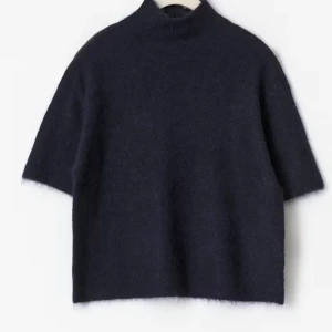 Mörkblå stickad tshirt - Snygg mörkblå stickad tshirtmed korta ärmar. Tröjan har en loose passform och är gjord i ett mjukt, fluffigt material som känns riktigt skönt mot huden. Perfekt för lager-på-lager och en stilren look. Den har inte polokrage!