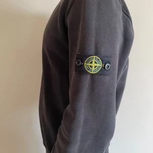  Stone Island sweatshirt - Svart sweatshirt från Stone Island med klassisk rund hals och ikonisk patch på vänster ärm. Perfekt för dig som gillar stilrena och snygga streetwear-plagg. 