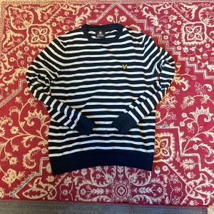Lyle & Scott sweatshirt - Snygg långärmad tröja från Lyle & Scott i marinblått och vitt med klassiska horisontella ränder. Tröjan har rund hals, ribbade muddar och den ikoniska gula loggan broderad på bröstet. Perfekt för en chill och stilren look.
