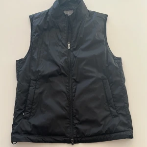Svart dunväst från Berkeley  - Svart dunväst från Berkeley i storlek S. Västen har två fickor framtill och stängs med dragkedja. Perfekt för lager-på-lager och enkel att matcha med olika outfits. Materialet är syntet och västen har en stilren, minimalistisk look. Nypris ca 1400kr | Pris kan diskuteras!!