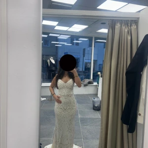 Beige klänning med vitapaljetter - Säljer en elegant beige  långklänning med glittrigt geometriskt mönster. Klänningen har smala axelband, v-ringad urringning och figurnära passform som framhäver siluetten. Materialet är glittrigt och känns lyxigt, perfekt för speciella tillfällen.  Klänningen finns i alla storlekar från XS-XL. Pris kan diskuteras.