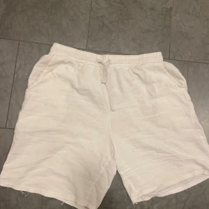 Vita linneshorts från King Billion - Säljer ett par fräscha vita shorts från King Billion i storlek L. De är tillverkade i svalt linne, har elastisk midja med snörning och två sidofickor. Perfekta för varma dagar när du vill ha en chill och stilren look.
