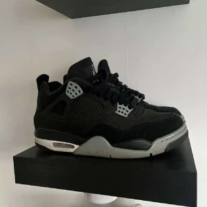Svarta Nike Jordan 4 sneakers - Säljer ett par svarta Nike Jordan 4 sneakers med grå detaljer och platt sula. Skorna har snörning och meshpaneler på sidorna, samt en robust design med synlig luftdämpning i sulan. Perfekta för dig som gillar streetwear och klassisk sneakerstil.