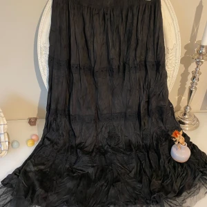 Svart långkjol  med spets  - Svart långkjol i tunn, skir bomull med  och spetsdetaljer. Kjolen har en lätt skrynklig look och faller snyggt med volym. Det finns underkjol och gummiband på midjan . .Perfekt för dig som gillar bohemisk stil och vill ha något luftigt och bekvämt.det finns ingen etikett på storleken,så den är som en smal även medium 