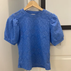 Blå spetsblus  - Säljer en blå blus som jag köpt från Vila fast som egentligen är från Object i storlek XS. Blusen har korta puffärmar och är gjord i ett vackert spetsmaterial med broderade detaljer och hålmönster. Rund halsringning och feminin passform, perfekt för dig som gillar unika toppar med snygga detaljer.
