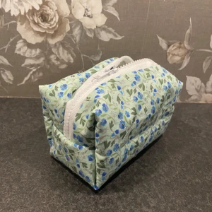 Blommig quiltad necessär med dragkedja - Egensydd, söt necessär i ljusgrönt tyg med blå blommor och gröna blad. Praktisk vit dragkedja upptill och rymlig boxig form, perfekt för smink eller småprylar. Mjuk och lätt, passar i väskan eller på resan.