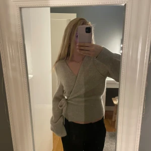 Beige omlottkofta med knyt i midjan - Supermysig beige omlottkofta med knyt i midjan och ballongärmar. Koftan är stickad och har en v-ringad pasform. Passer perfekt till hösten. Är i nytt skick