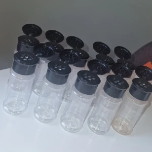 Plastburkar med svart lock, 10-pack - 10 st transparenta plastburkar med svart lock och hål för ströning, perfekta för kryddor och torrvaror. Burkarna är använda under kort tid men diskade, en burk är fortfarande är röd av chili pulver då jag inte hade en borste som fick plats i de för att kunna skrubba. Alla burkar är i mycket fint skick, inga defekter eller slitage. 