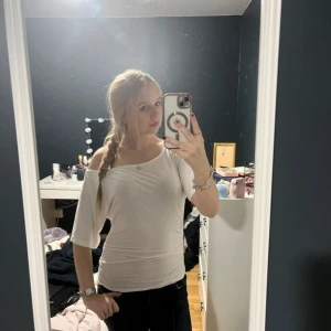 Vit offshoulder topp - Säljer en vit offshoulder topp med trekvartsärm. Toppens passform är tight och den har en enkel, stilren design utan mönster eller detaljer. Perfekt för dig som gillar en clean och fräsch look.