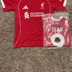 Alexander isak number 9 liverpool 25/26 - Riktigt snygg Liverpool fotbollströja från Adidas i röd färg med vita detaljer. Kortärmad modell med tryck 'ISAK' och nummer 9 på ryggen. LFC-logga och Standard Chartered sponsor på bröstet. Slim fit och tillverkad i lätt, ventilerande polyester. Fråga inte för mått.