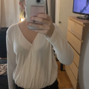 Vit omlottopp från Bik Bok XS - Säljer en vit omlottopp från Bik Bok i storlek XS. Toppen har lång ärm, v-ringning och resår i midjan för en snygg passform. Materialet är mjukt och stretchigt, perfekt till jeans eller kjol. Enkel och stilren design som funkar året runt. Super skön tröja! Skriv vid fler frågor💕