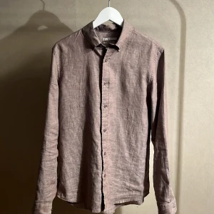 Beige linneskjorta från Cubus - Stilren beige skjorta i linne från Cubus med klassisk krage och knäppning framtill. Skjortan har lång ärm och en avslappnad passform, perfekt för en chill och snygg look. Enkel att matcha med både jeans och chinos.