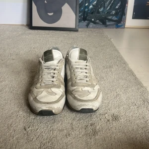 Valentino Rockrunner sneakers i beige - Snygga Valentino Rockrunner sneakers i beige och grått med camouflage-mönster. Skorna har snörning, platt sula och detaljer i mocka och skinn. Ikoniska nitar på hälen och rund tå ger en cool vibe. Perfekt för dig som gillar exklusiva streetwear-sneakers.