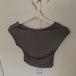  croppad topp från Bershka - Säljer en croppad topp från Bershka i storlek S. Toppen har en bred, rundad halsringning och är ärmlös med en tight passform. Materialet är mjukt och stretchigt, perfekt för att styla med jeans eller kjol. Enkel och clean design som ger en snygg siluett. (Dåligt ljus så på andra bilden visar hur färgen ser ut på riktigt). 