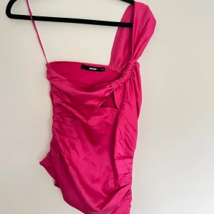 Rosa asymmetrisk klänning Bik Bok - Säljer en topp från Bik Bok med asymmetrisk design och rynkade detaljer. Toppen har ett brett axelband på ena sidan och ett smalt på andra. 