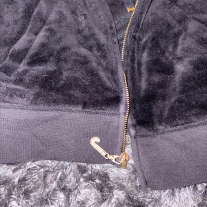 Svart Juicy Couture kofta - Svart velourjacka från Juicy Couture med huva och dragkedja i guld. Jackan har långa ärmar, ribbade muddar och fickor framtill. Klassisk slim passform och ikonisk JC-detalj på dragkedjan. 💗 Nypris 1.300kr
