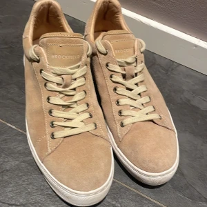 Beige mocka sneakers från Brockfield - Snygga beige sneakers från Brockfield i mjuk mocka med vita snören och vit platt sula. Klassisk rund tå och stilren design som passar till jeans eller shorts. Perfekt för dig som gillar neutrala färger och enkel stil.