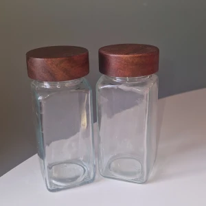 Glas kryddburkar - Två kryddburkar med trälock och plastinsats för ströfunktion-perfekta för kryddor eller torrvaror. Burkarna är nya utan synligt slitage eller defekter. Stilren design som passar i de flesta kök.