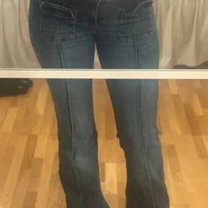 Blå jeans med fickdetaljer - Snygga blå jeans med unika fickdetaljer framtill. Byxorna har en bootcut-stil och är perfekta för en avslappnad look. De har en klassisk jeansfärg och är tillverkade i ett bekvämt material.