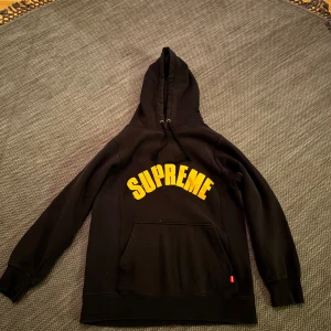 Supreme hoodie - Säljer en supreme hoodie i svart med simpelt gult tryck över bröstet. Den är köpt secondhand hand men är i bra skick😊 Skriv vid mer funderingar mm