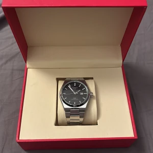 Tissot PRX Powermatic 80 herrklocka - Snygg Tissot PRX Powermatic 80 herrklocka med svart urtavla och datumvisning. Klockan har ett stilrent silverfärgat armband i rostfritt stål och kommer i en elegant röd förpackning. Perfekt för den som söker en tidlös och elegant accessoar. Har fler bilder om det sökes! Pris kan diskuteras vid snabb affär 