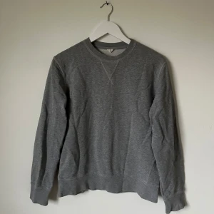Grå sweatshirt från Arket - En stilren grå sweatshirt från Arket i storlek S, tillverkad av extra-lång bomull. Tröjan har rund hals, ribbade muddar och klassisk passform. Perfekt för chill dagar och enkel att matcha med jeans eller joggers. 5I10