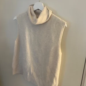 Beige stickad väst med polokrage Amisu - Säljer en beige stickad väst från Amisu i storlek L. Västen har en bred, ribbad polokrage och är ärmlös med rak passform. Materialet är mjukt och ger en chill vibe, perfekt att styla över en långärmad tröja. Enkel och clean design utan mönster. Passar S