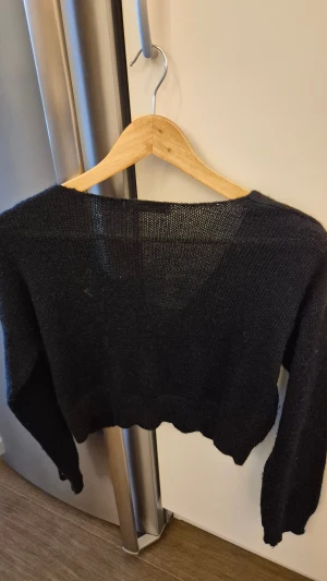 Svart stickad tröja NA-KD - Svart stickad tröja från NA-KD med djup v-ringning och lång ärm. Tröjan är mjuk och har en loose passform, perfekt för lager-på-lager. Materialet är 80% akryl och 20% polyamid, vilket gör den lätt och skön att bära.