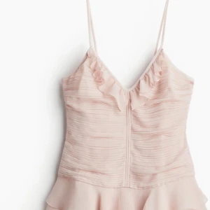 Ljusrosa volangklänning från H&M - Supersöt ljusrosa kortklänning från H&M med tunna axelband, v-ringning och volangdetaljer både upptill och nertill. Helt ny med prislapp kvar. Passar även S då de liten i storlek 