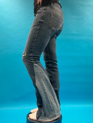 Blå bootcut jeans med slitningar - Storlek 27/32, innerbenslängden 78 och midjemåttet 38💙 Snygga blå bootcut jeans med slitningar och dubbla knappar i midjan. Jeansen har klassiska fem fickor, markerade sömmar och lätt tvättad look. Materialet är jeans med stretch och passformen är normal med utsvängda ben. 