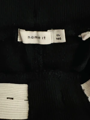 Svarta mjukisbyxor  - Svarta mjukisbyxor med ribbade muddar och grå snörning i midjan. Byxorna har en slim passform och är perfekta för chill dagar. Materialet är mjukt och bekvämt, vilket gör dem sköna att ha på sig hela dagen.