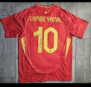 Spansk landslagströja Lamine Yamal #10 - Säljer en officiell röd EM Spanien fotbollströja med gula detaljer, nummer 10 och Lamine Yamal på ryggen. Tröjan har korta ärmar, meshpaneler i sidorna och är tillverkad i lätt polyester. Tryckt landslagsemblem på bröstet och autograf på siffran. Beckett QR certifikat som bekräftar tröjans äkthet !