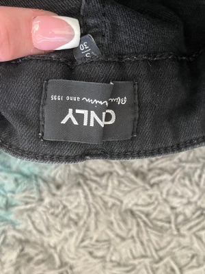 Svarta bootcut jeans från ONLY - Svarta jeans från ONLY med klassisk femficksdesign och bootcut-ben. Högmidjade och tillverkade i stretchigt bomullsmaterial för skön passform. Snyggt svarta med subtila slitningar framtill, perfekta för en cool och avslappnad look.